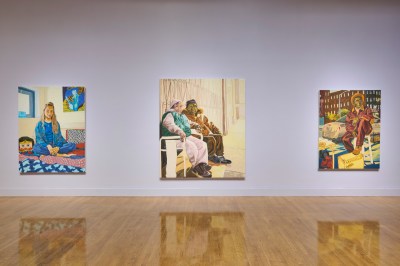 Three painted portraits by the same artist hang on a museum wall that is painted lavender. 