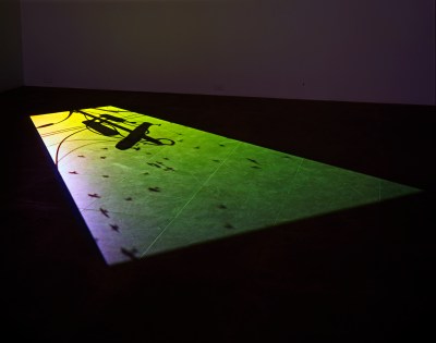 A projection on a darkened floor showing a telephone pole and falling debris.