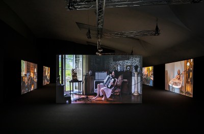 A multiscreen video installation showing people playing music in different rooms of a house.