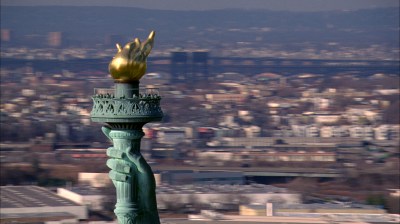 The Statue of Liberty's torch in front of a blurred cityscape.