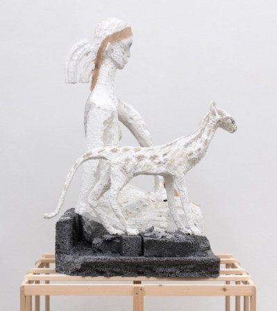 A girl sculpture of a girl kneeling next to a slender cat on a wooden armature.
