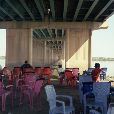 Several brightly colored chairs (in red, pink and blue) are combined together. Several people sat under them.