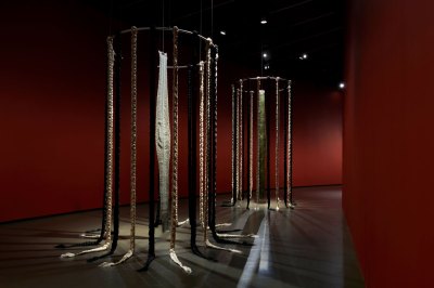 Two large devices can be seen, made of braids and a piece of leather hand. They are installed in a red curved gallery. 