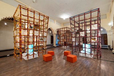 View of three sculpture installations in the museum. They are made of colorful fabrics similar to cubic grids. The tapestry is embedded in some squares, with the center of each block being a TV screen. 