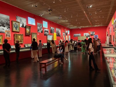Installation view of the museum gallery with red painted walls showing various objects on the walls and glass. 