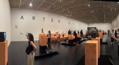 The museum exhibition displays traditional works of African art. All kinds of people look at them. 