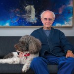 A man sitting on the sofa with an abstract painting of a poodle underneath.