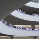 Partial view of the rotunda with LED screen showing text hanging on its white walls. See “Evacuate from me” on one floor, doubled the letters.