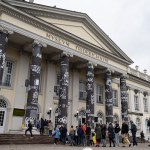 A group of people walked into the museum, surrounded by pillars around the banner.
