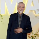 A man in suit in front of the MOMA logo.