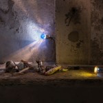 A doll made of reused materials is located on a concrete bench lit by a light bulb.