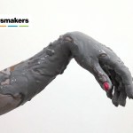 A limp hand with pink nails is in the middle of the frame, covered in a gray viscous substance.
