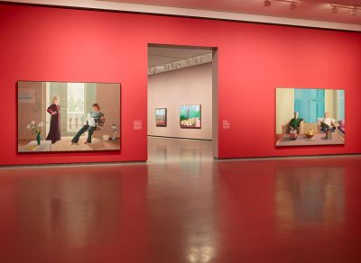 The wall in front of the entrance way has a view of the gallery with vermilion walls and two double portraits. 