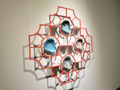 A work that embeds four ceramic shell vessels into an orange-painted metal architectural element.