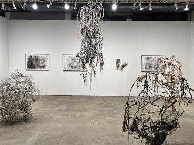 Several intricate sculptures made from  electrical wire and silk organza hang in the center of an art fair booth.
