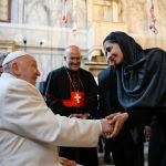 A man in a pope robe greets him in a black turban.