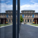A museum's buildings and square reflect in glass panes.