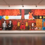 A large-scale painting shows a squatting red figure, surrounded by other characters, satellites, red scraps, and more.