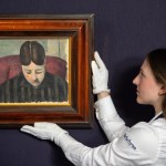 A woman in white gloves holding a woman's painting on the wall.