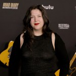 A woman stands on the red carpet in front of two guitars.