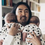 A Japanese man with long hair is holding twins.