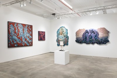 Some abstract artworks hang on white wall. The center is a sculpture of a Korean stewardess.