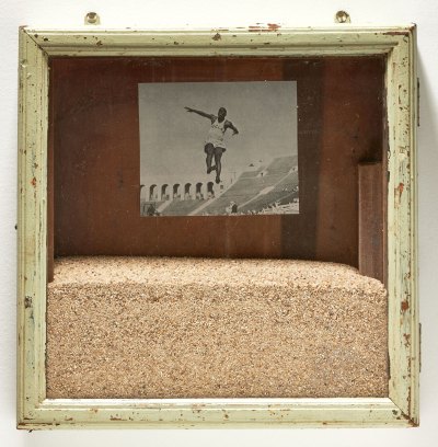 A frame with sand a photo of a Black UCLA athlete in mid jump. 