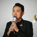 A man standing in front of a banana tube on the wall holding a microphone.