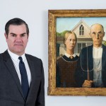 A man in a suit stands next to a farmer with a pitchfork next to a woman in front of the house.