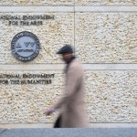 A person walks on a building and there are signs of the state of the National Arts and Humanities Foundation.