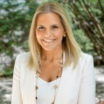 A smiling blonde woman wearing a white jacket and top.