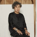 A woman sitting on a stool in front of a white canvas.