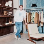 Portrait of Jonathan Anderson in a Loewe retail store. He was wearing a crew sweater and light jeans, leaning against a wooden chair.