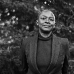 A black and white photo of a black woman standing among trees.