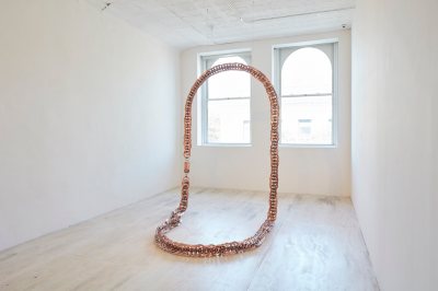 A necklace-like sculpture stands in the gallery.
