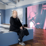 A woman sitting on the platform in front of a video monitor.