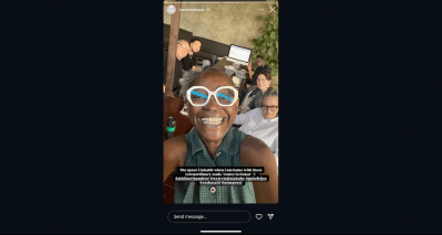A black woman takes a selfie with five other people and sits on the table behind her.