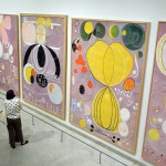 A woman stares at four large abstract paintings.