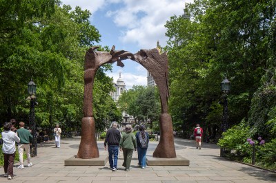 A large bronze sculpture, similar to two wooden blocks, forms a gate in the park.