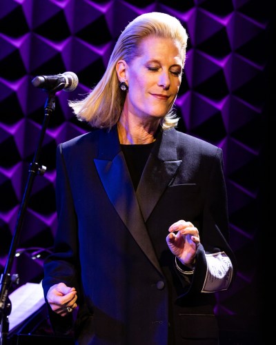 A blonde woman is on a microphone and sticks out her fingers.
