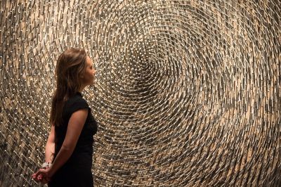 A woman stands in front of a work made of spiral nails.