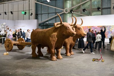 A small red scooter stands in front of the wooden sculpture of two cows, pulling two wheels.