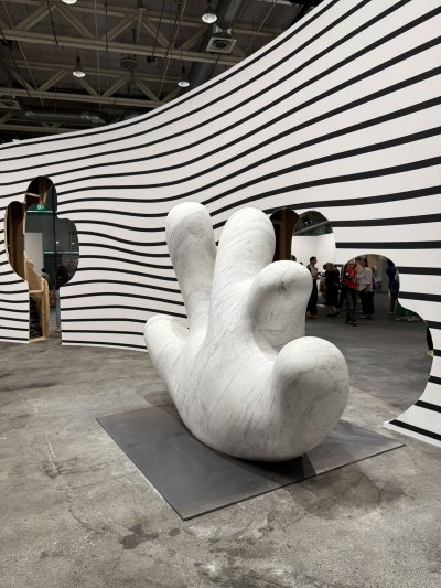 A curved black and white striped wall with cuts on it and a marble cactus in front.
