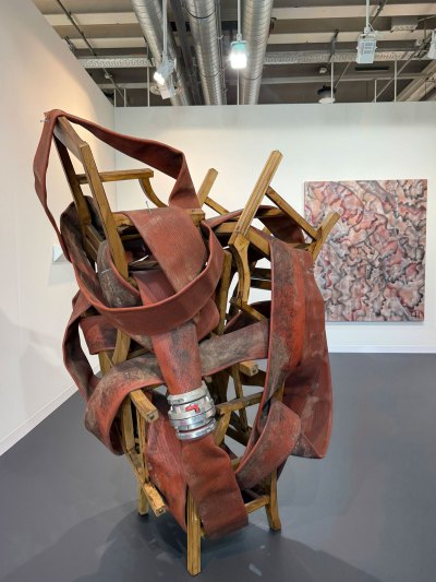 Sculpture of red fire hoses intertwined with various stacked wooden chairs.