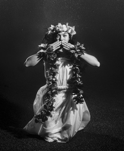 A local Hawaiian woman in Hawaii dressed in white and photographed underwater while taking pictures in the woods, making a welcome gesture. 