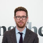 A red-haired man with beard and glasses smiling for the camera.