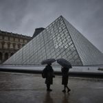 On a rainy day, two people covered their umbrellas in a rainy day next to the glass pyramid structure.