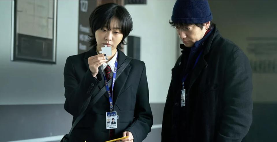 Woman holds up puzzle. A man in a winter coat and beanie looked at her. They both wore police ID cards.