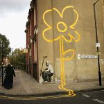 A woman walks through a painting of yellow flowers on the wall on the street.