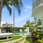 The facade of the house and a swimming pool surrounded by palm trees.